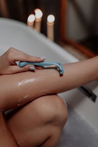 Woman shaving legs in a candlelit bath — summer hair removal methods and self-care concept
