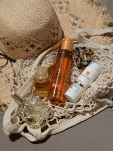 Stylish flat lay of beach bag essentials including a straw hat, sunscreen, and perfume for summer relaxation.