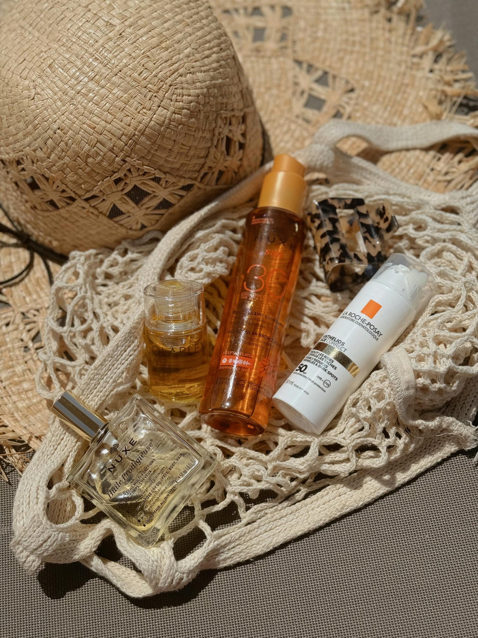 Stylish flat lay of beach bag essentials including a straw hat, sunscreen, and perfume for summer relaxation.